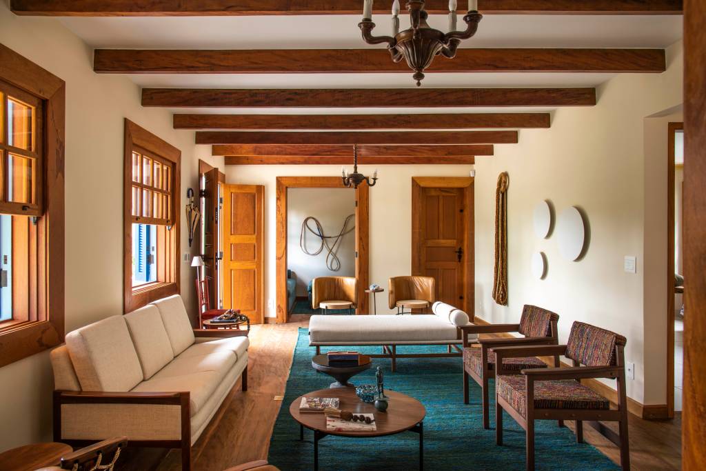 3-retrofit-em-duas-casas-de-familia-recupera-estilo-colonial-das-construcoes Sala de estar com vigas de madeira, sofá branco e cadeiras marrons e tapete turquesa