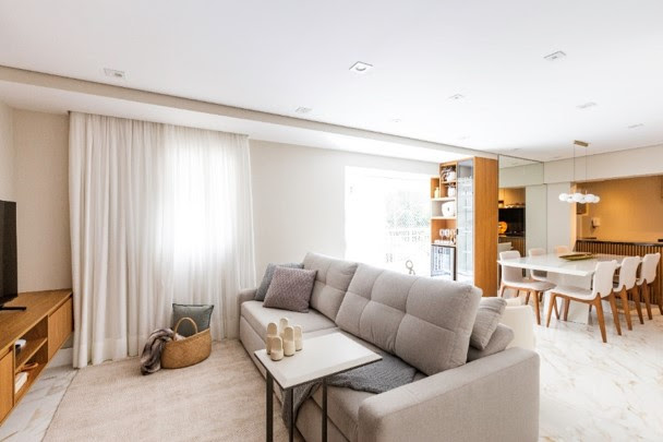 sofa-retratil-sofa-ilha-diferencas-onde-usar-dicas-para-escolher-02-daniela-funari Sala de tv com tapete bege, cortinas brancas e sofá cinza retrátil.
